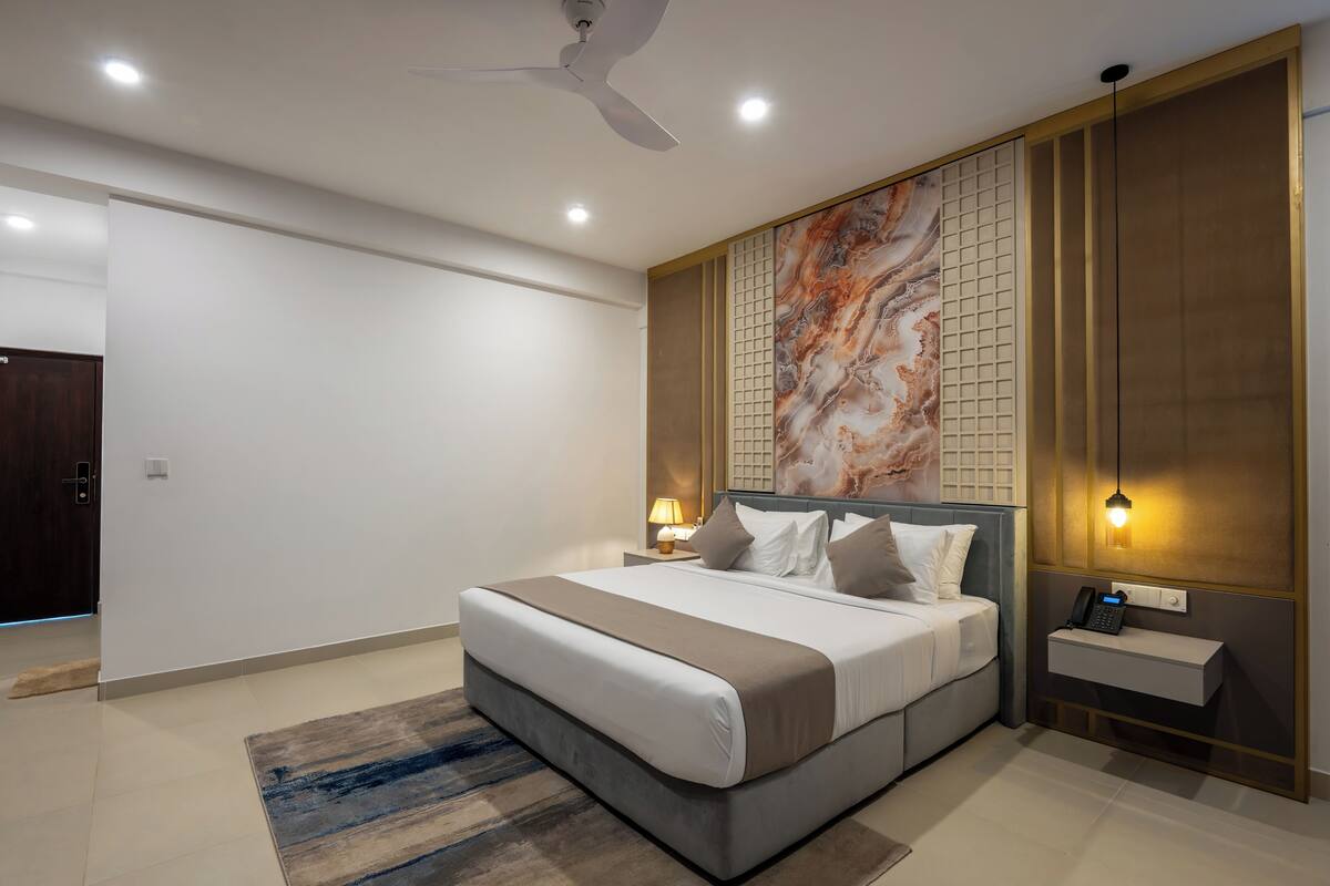 A modern bedroom with a large bed, bedside lamps, a phone, and a decorative wall panel.