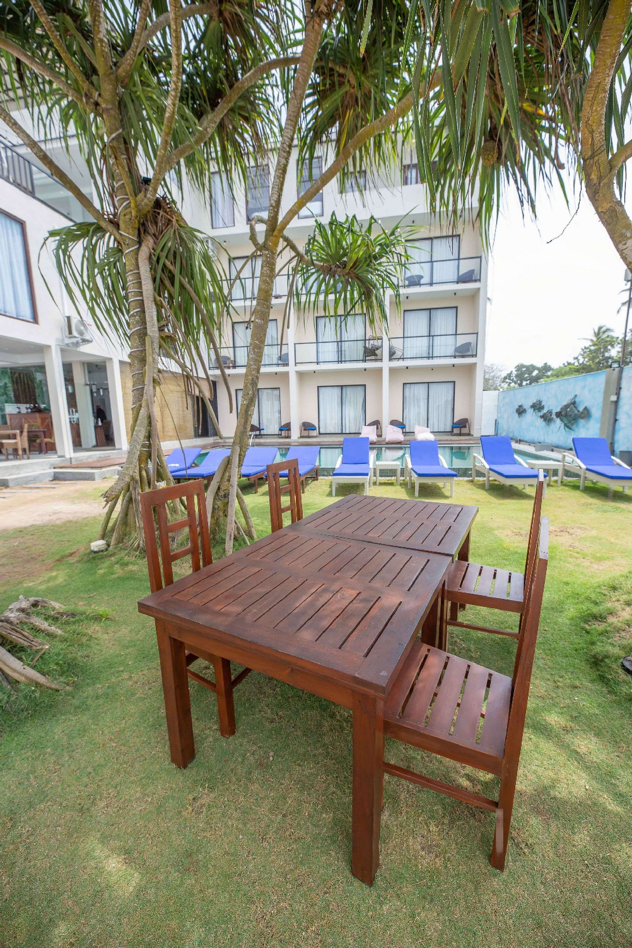 A wooden table and chairs set outdoors with a pool and lounge chairs in the background.