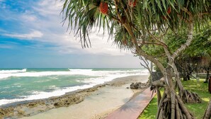 Una playa con un paseo de madera, palmeras y olas del océano.
