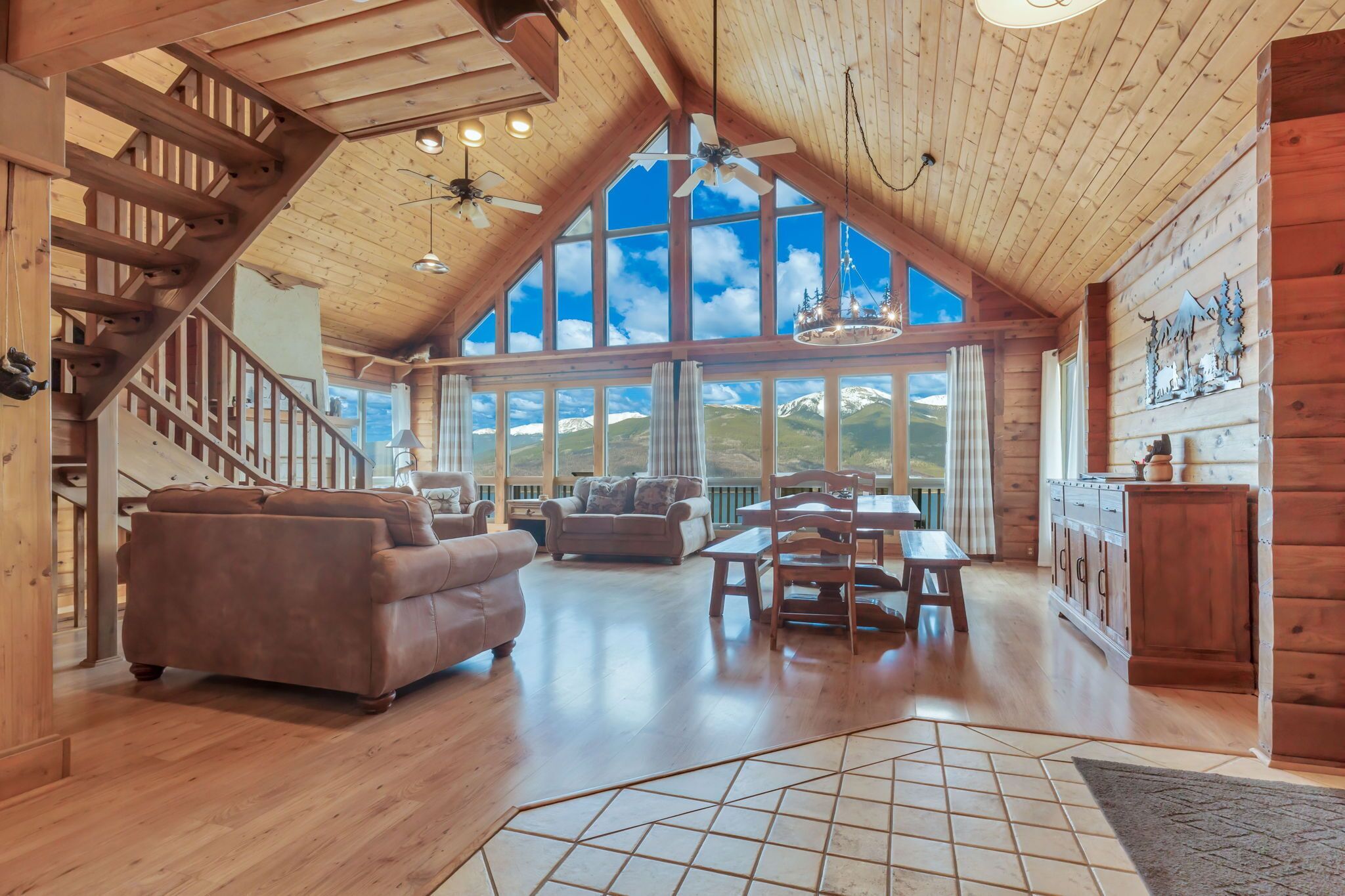 Amplia sala de estar con pisos de madera, una escalera y ventanas grandes que ofrecen vistas a las montañas.