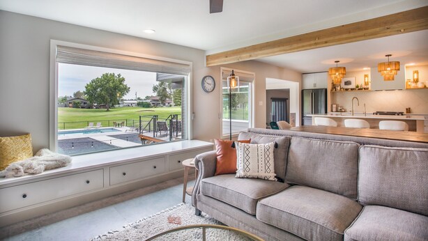 Ein modernes Wohnzimmer mit großem Fenster, das einen Pool und einen Golfplatz überblickt.