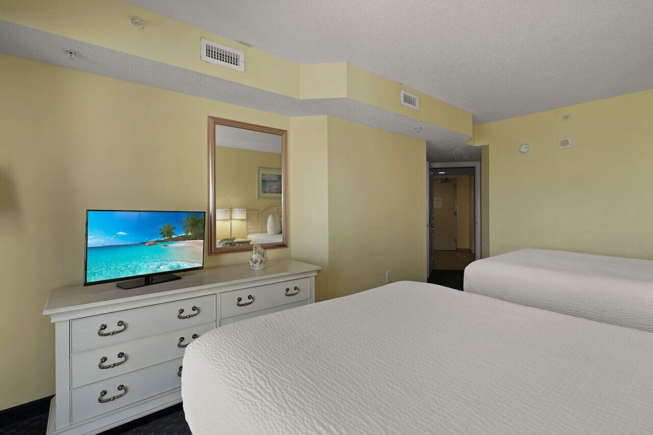 A hotel room with a bed, a TV on a dresser, a mirror, and a door leading to a bathroom.