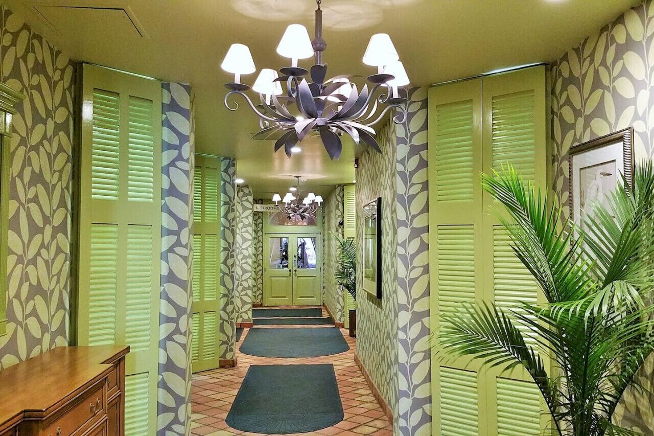 Un pasillo con papel tapiz estampado, un candelabro, un banco de madera y una planta en maceta.