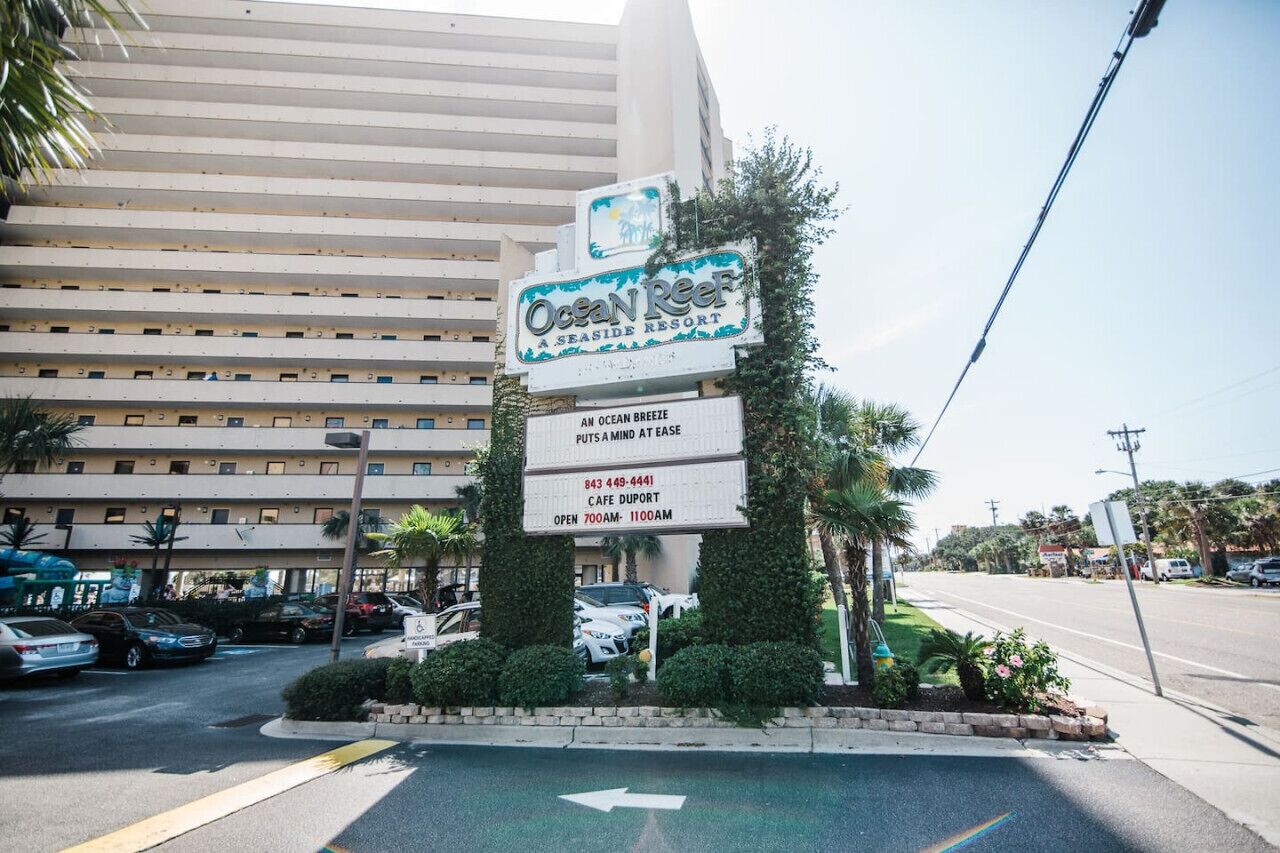 A sign for Ocean Reef A Seaside Resort with a cafe and restaurant, and a parking lot with cars.