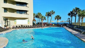 A swimming pool with lounge chairs and palm trees, surrounded by a building with balconies. - 4BR oceanfront, 8th fl, big balcony in Ocean Reef (Myrtle Beach)