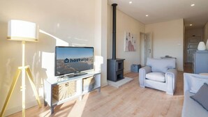 Een moderne woonkamer met een televisie, een bank, een fauteuil, een lamp en een houtkachel.