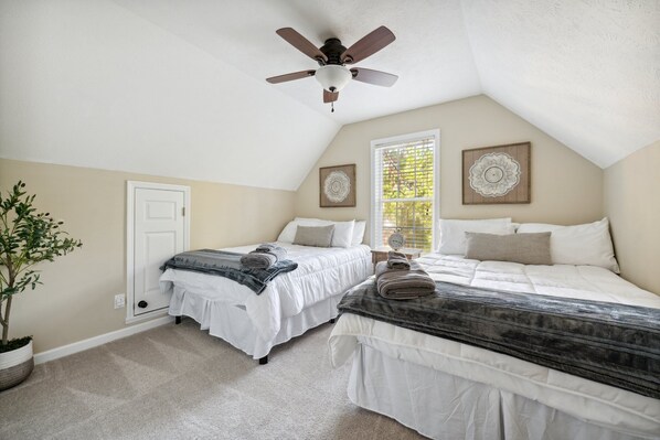 A bedroom with two beds, a ceiling fan, a potted plant, and two decorative wall pieces.