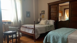 Ein Schlafzimmer mit zwei Betten, Holzboden, einem Stuhl und einem Fenster mit Vorhängen.