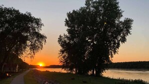 Ein Sonnenuntergang mit einem Pfad, Bäumen und einem Gewässer.