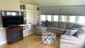 A living room with a flat-screen TV, wooden cabinet, beige sectional sofa, and a round coffee table.