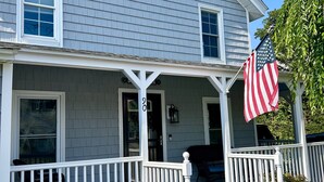 A two-story house with a porch, a front door, and an American flag.