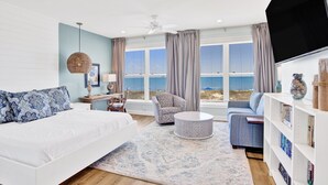 A modern living room with a large bed, a sofa, a chair, a round coffee table, and a bookshelf. - Gulf-Front Duplex | Pet Friendly | Pools and Pier Access (Gulf Shores)