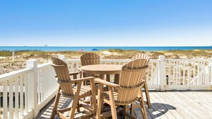 A wooden deck with a table and chairs overlooking a beach. - Gulf-Front Duplex | Pet Friendly | Pools and Pier Access (Gulf Shores)