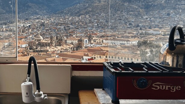 Cuina amb rentatge, aixeta i fogó, amb vista a un paisatge urbà i muntanyes de fons.