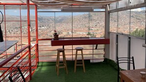 Habitació amb vista a un paisatge urbà, una barana vermella, un tamboret de fusta i una taula amb una tassa.