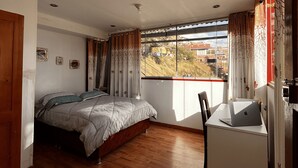 Un dormitori amb un llit, un escriptori amb un ordinador portàtil, una finestra amb cortines i vista a l'exterior.