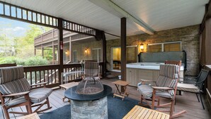 Un patio techado al aire libre con un hogar de piedra, muebles de madera y un jacuzzi.