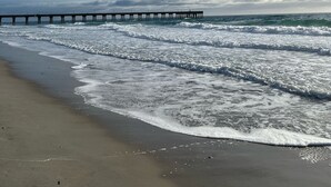 A beach with waves, a pier, and a cloudy sky.