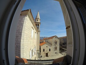 Une vue à travers une fenêtre circulaire d’un bâtiment historique doté d’un clocher et d’une façade en pierre.