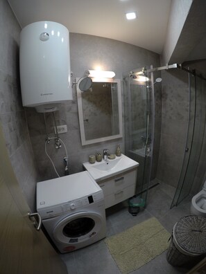 A modern bathroom with a built-in washing machine, a glass-enclosed shower, and a vanity with a mirror and sink.