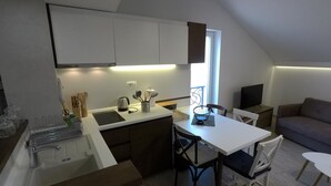 Eine kompakte Küche mit weißen Schränken, einem Esstisch und einer Couch in einer Loft-Wohnung.