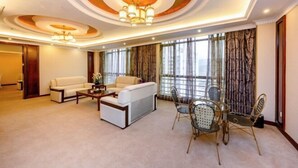 A spacious living room with a sofa, coffee table, and dining set. The room features a large window with curtains and a chandelier. - Shengjing Hotel (Fuyuan)