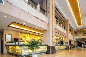 Rebedor d'hotel amb taulell de recepció de marbre, diverses plantes i una escala.