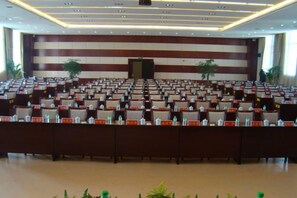 A conference room with rows of chairs, a podium, and potted plants. - Shengjing Hotel (Fuyuan)