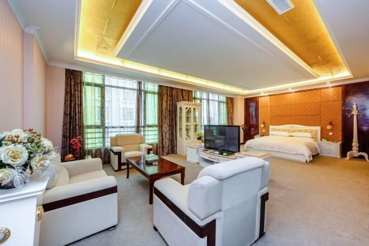 A hotel room with a large bed, a TV, a sofa, and a desk.