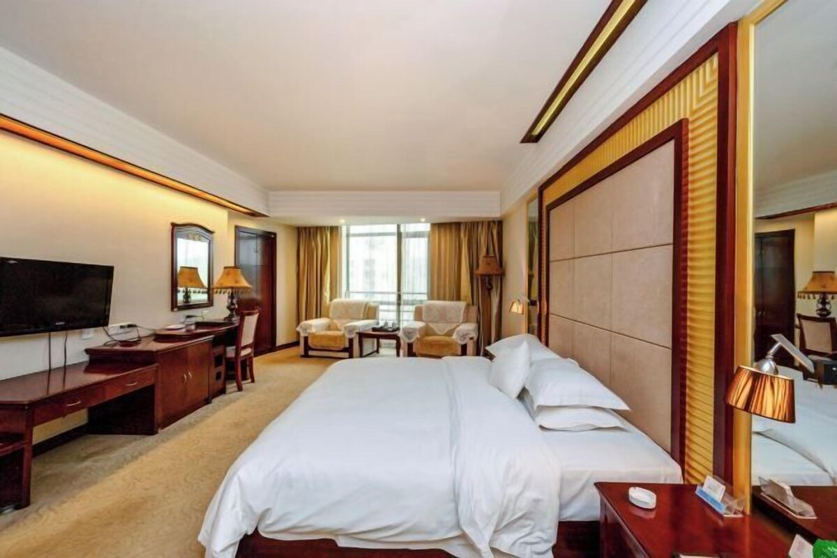 A hotel room with a large bed, a desk, a TV, and a seating area with chairs.