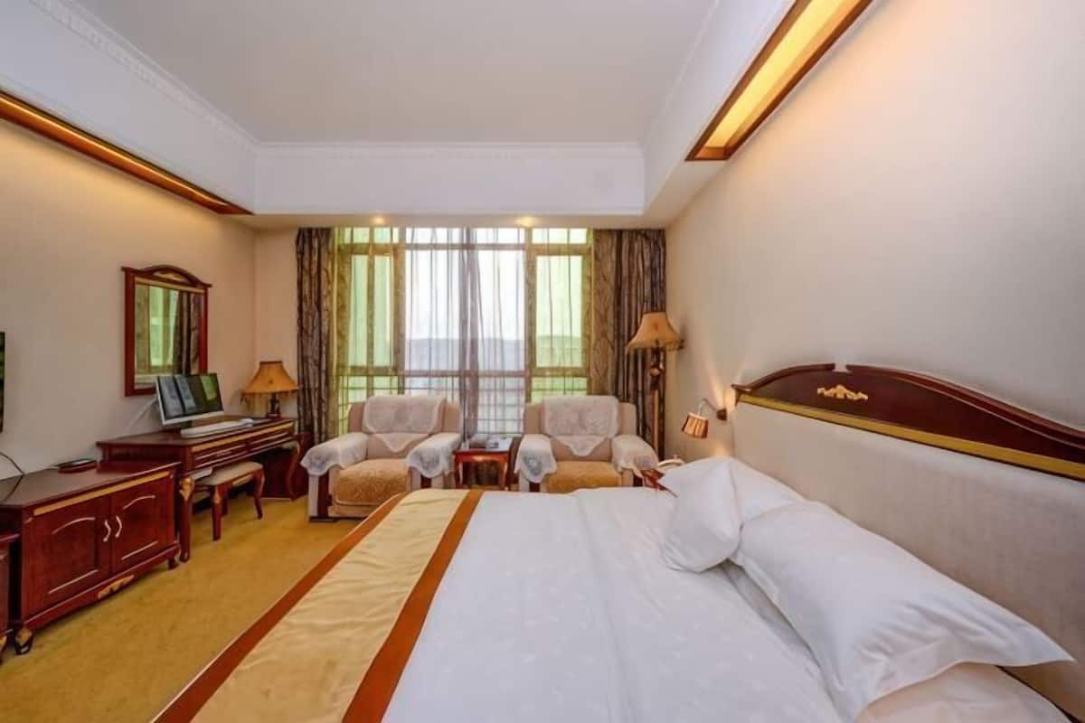 A hotel room with a large bed, two armchairs, a desk, and a television.