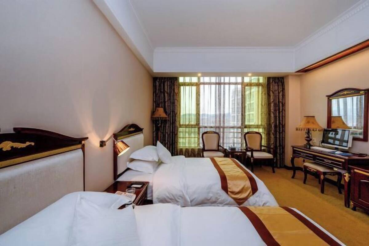 A hotel room with two beds, a desk, a chair, and a television.