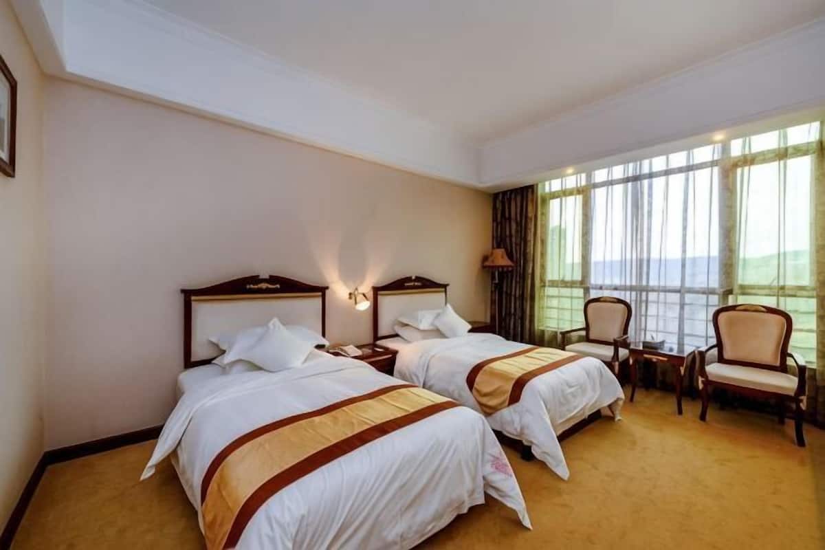 A hotel room with two beds, a small table, two chairs, and a large window.