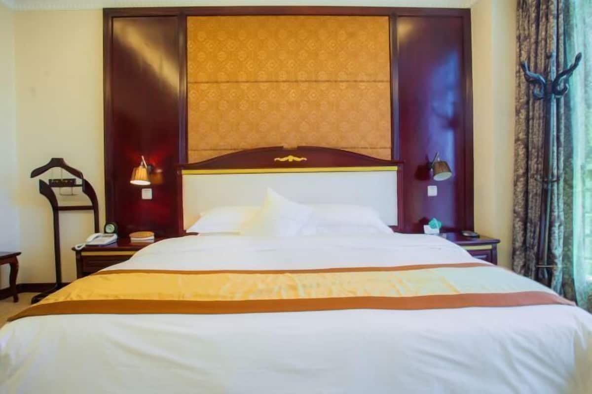 A hotel room with a large bed, a wooden headboard, a bedside table with a lamp, and a nightstand with a phone.