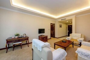 A living room with a TV, a wooden desk, a bench, and two armchairs. - Shengjing Hotel (Fuyuan)