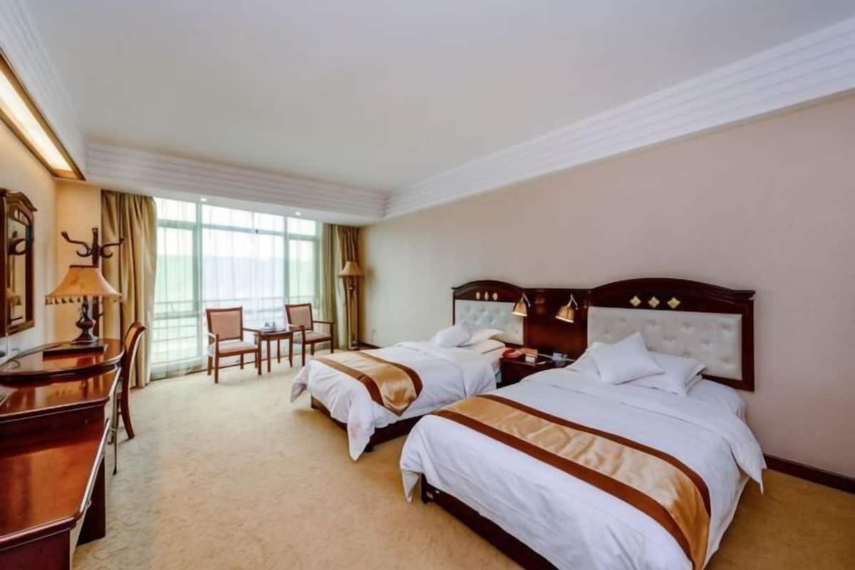 A hotel room with two beds, a desk, chairs, and a large window.