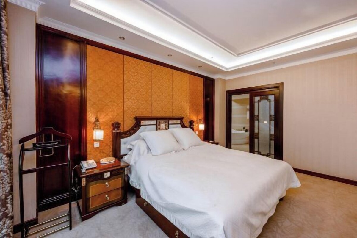 A hotel room with a large bed, wooden headboard, bedside lamps, a nightstand, and a mirror.
