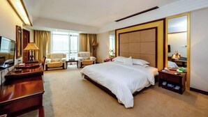 A hotel room with a large bed, a desk with a lamp, two armchairs, a TV, and a large mirror. - Shengjing Hotel (Fuyuan)