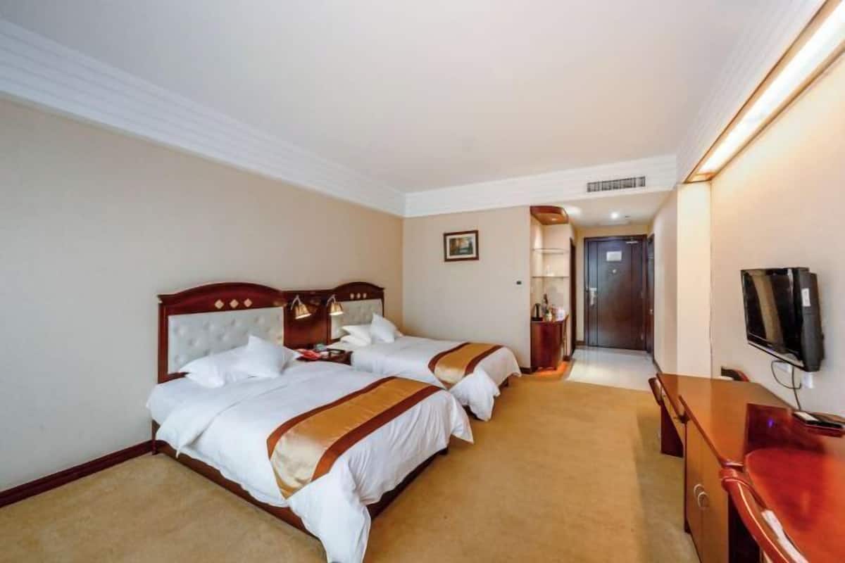 A hotel room with two beds, a TV, a desk, and a bathroom visible through an open door.