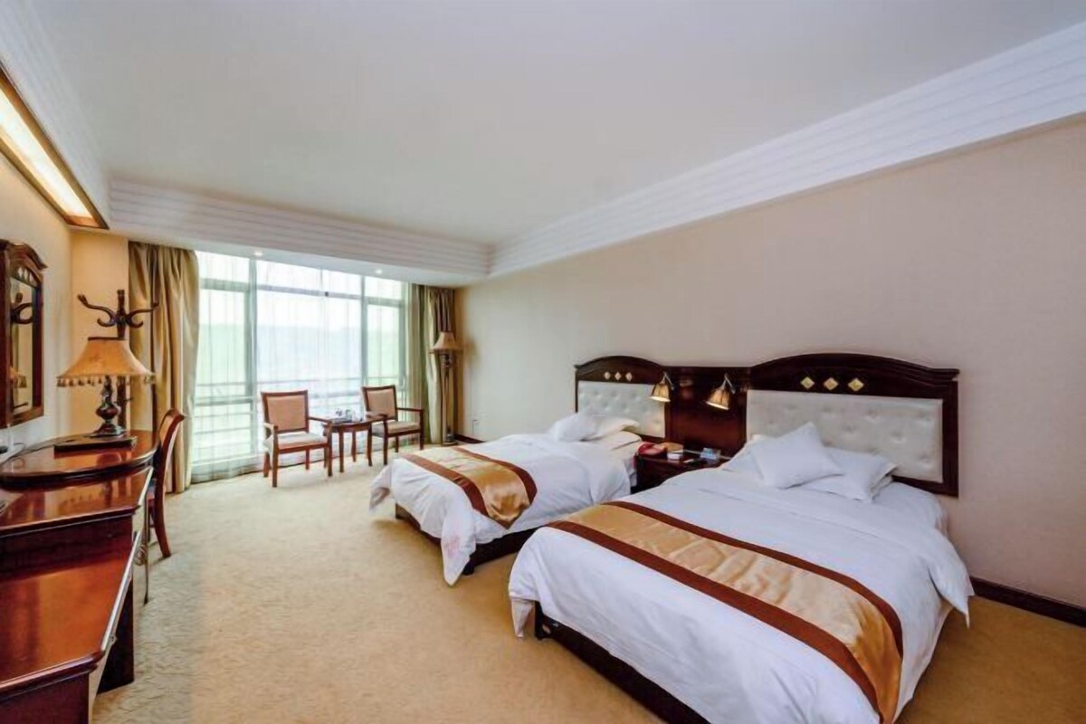 A hotel room with two beds, a desk, a chair, and a large window.