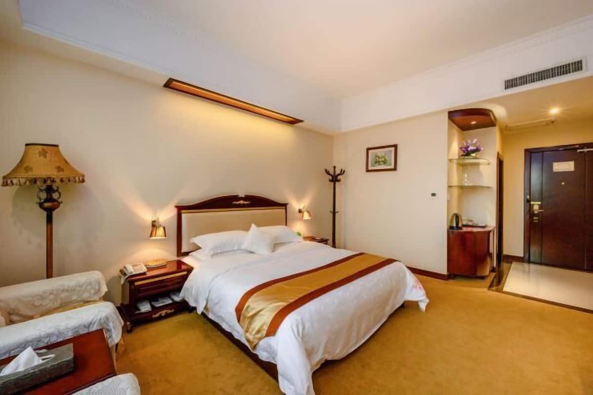 A hotel room with a large bed, bedside tables, a lamp, a coat rack, and a door.