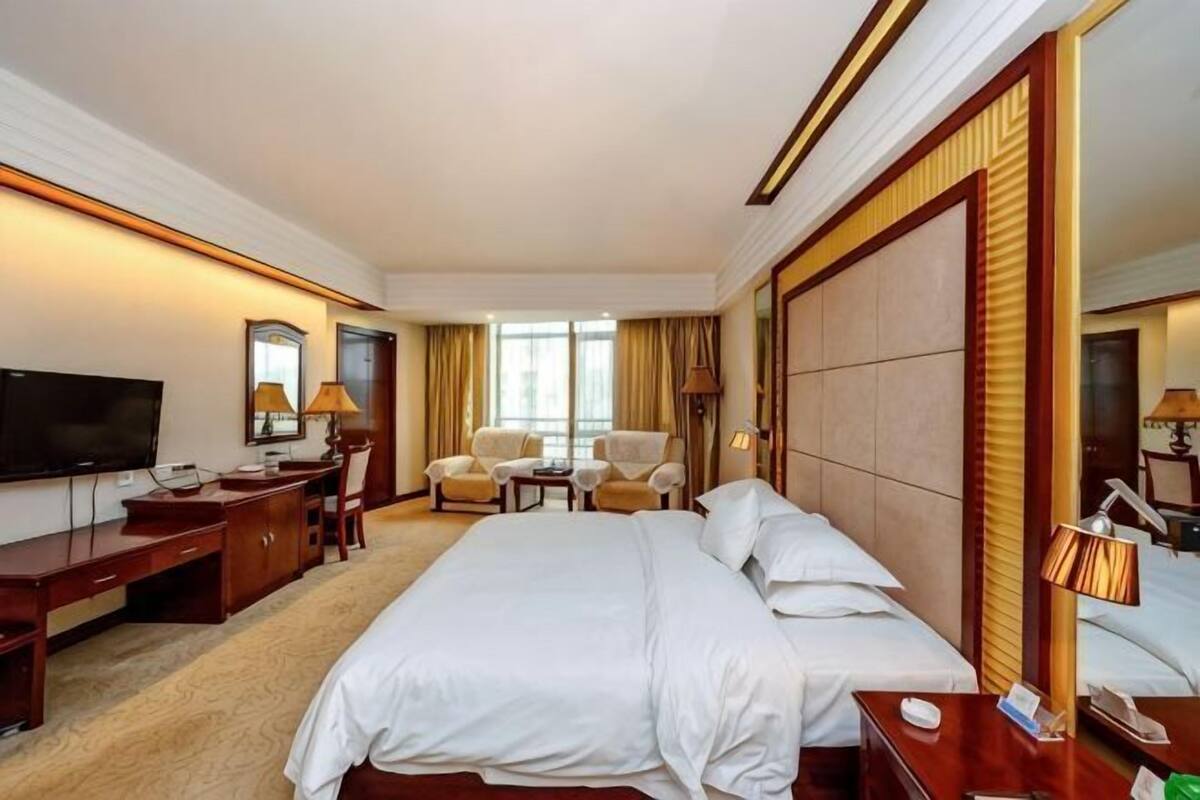A hotel room with a large bed, a desk, a chair, a TV, and a window.
