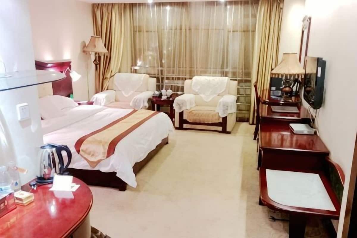 A hotel room with a bed, two chairs, a desk, a TV, and a mirror.