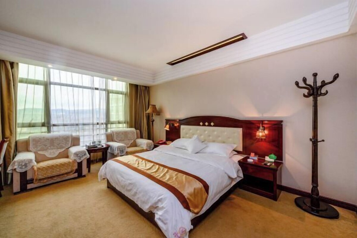 A hotel room with a large bed, two armchairs, a nightstand, a lamp, and a coat stand.