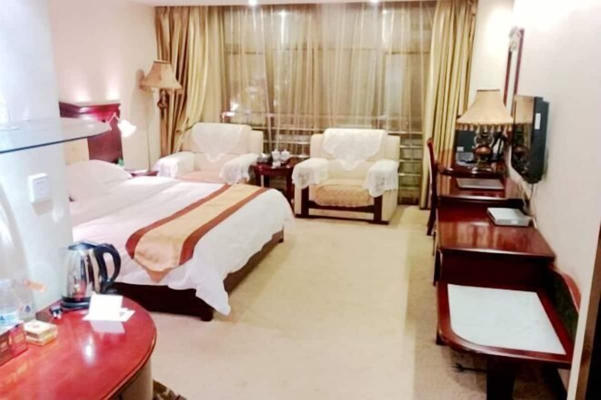 A hotel room with a bed, two chairs, a desk, and a television.