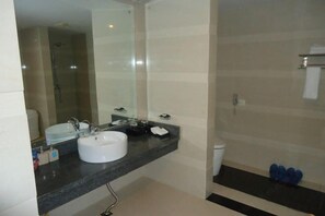A bathroom with a white sink, a mirror, a shower, and a toilet. - Shengjing Hotel (Fuyuan)