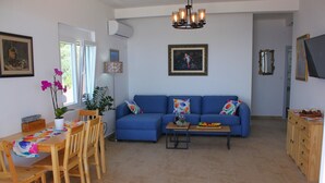 Uma sala de estar com sofá azul, mesa de jantar de madeira, cadeiras, uma pequena mesa de centro e um vaso com planta.