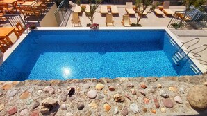Piscina com área de deck revestida, rodeada por espreguiçadeiras e mesas.