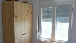 Quarto com duas camas, um guarda-roupa de madeira, uma mesa de cabeceira com abajur e uma janela com persianas.