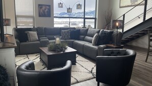 A modern living room with a large window, a sofa, a coffee table, and a staircase. - MT Luxury! (Bozeman)